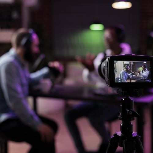 Multiethnic team of people meeting to broadcast internet podcast, recording video discussion on camera. Influencer and guest talking on online livestream to create social media channel content.